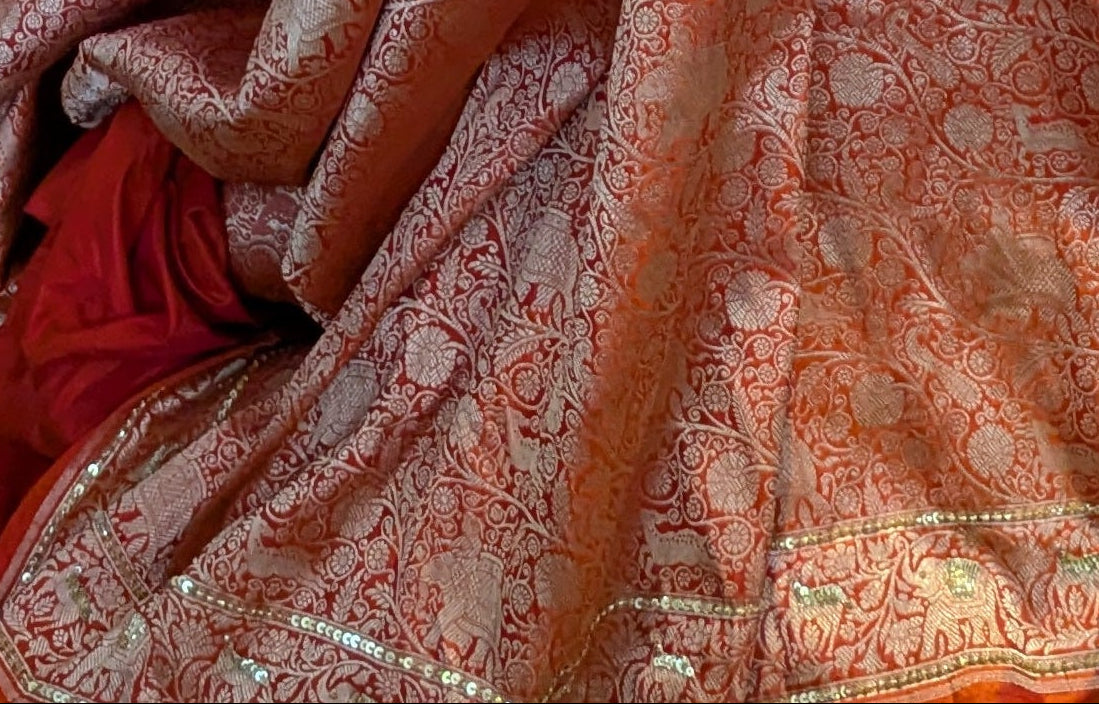 Orange saree with gold patterns draped over a stand against a textured wall.